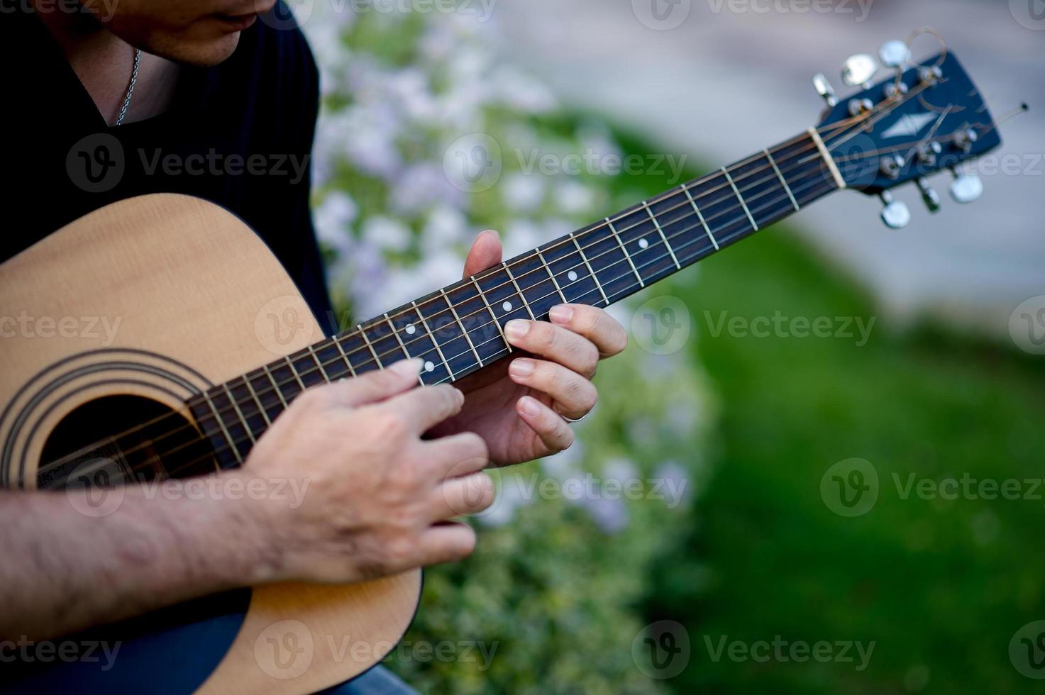 immagine di un chitarrista, un giovane che suona una chitarra mentre è seduto in un giardino naturale, concetto musicale foto