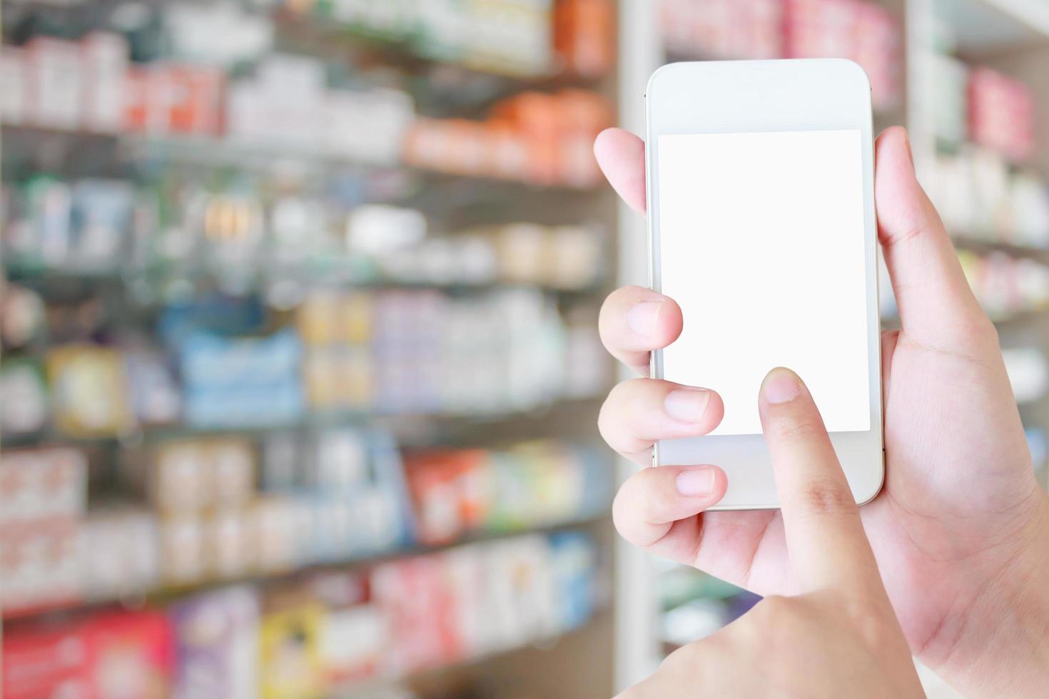 smartphone mobile con schermo vuoto della tenuta della mano della donna sopra la medicina sugli scaffali dei negozi della farmacia foto