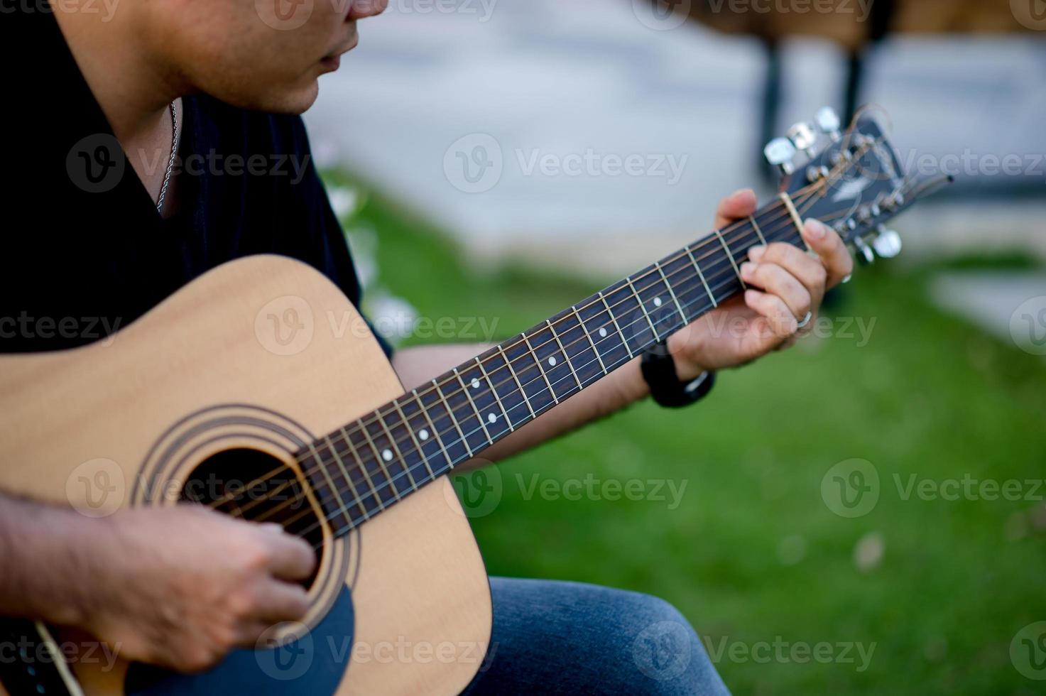 immagine di un chitarrista, un giovane che suona una chitarra mentre è seduto in un giardino naturale, concetto musicale foto