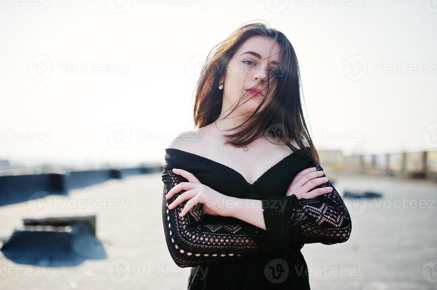 ritratto bruna ragazza con labbra rosse che indossa un abito nero poste sul tetto. modello di moda di strada. foto