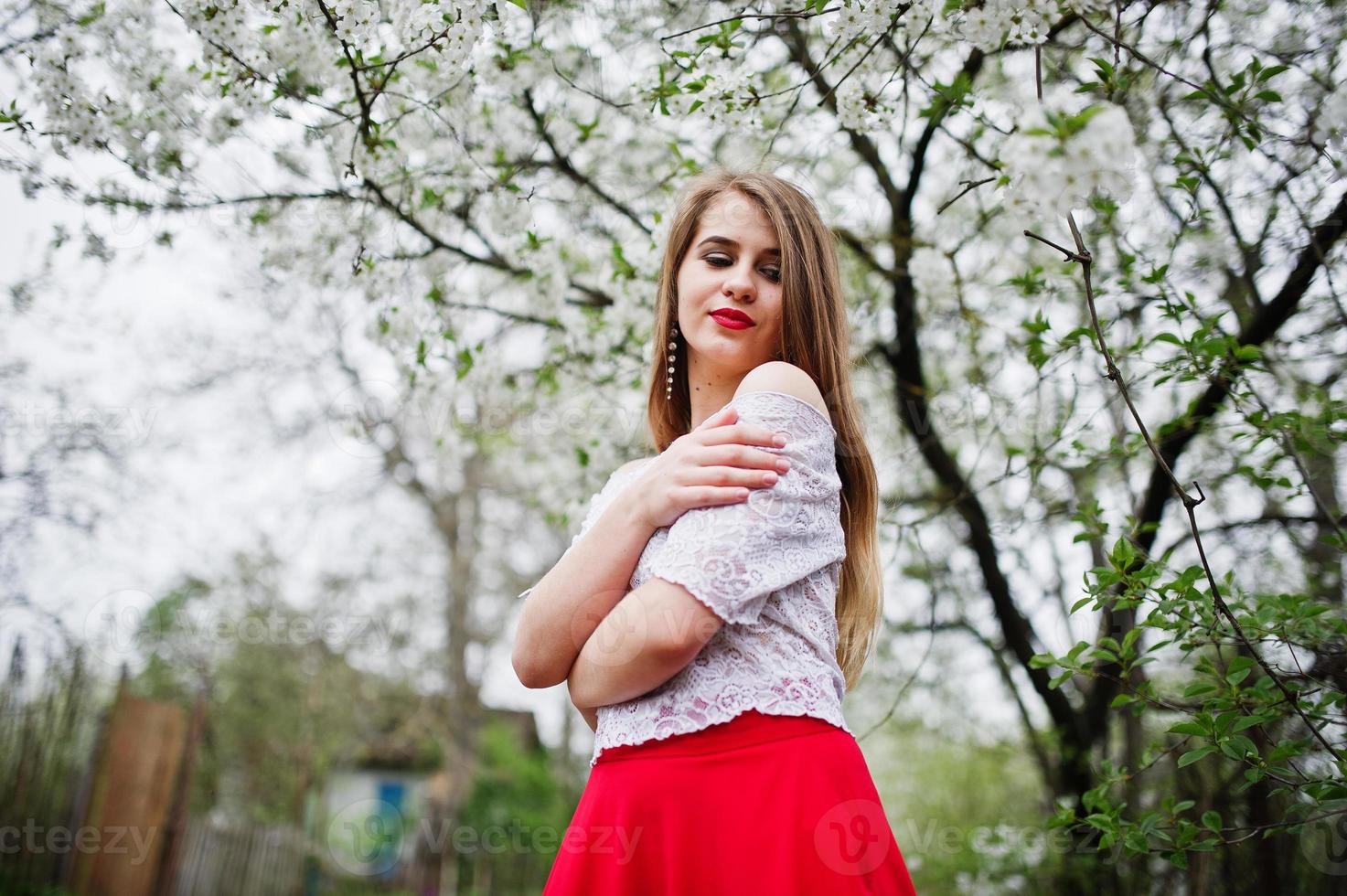 ritratto di bella ragazza con labbra rosse al giardino di fiori primaverili, indossare su abito rosso e camicetta bianca. foto