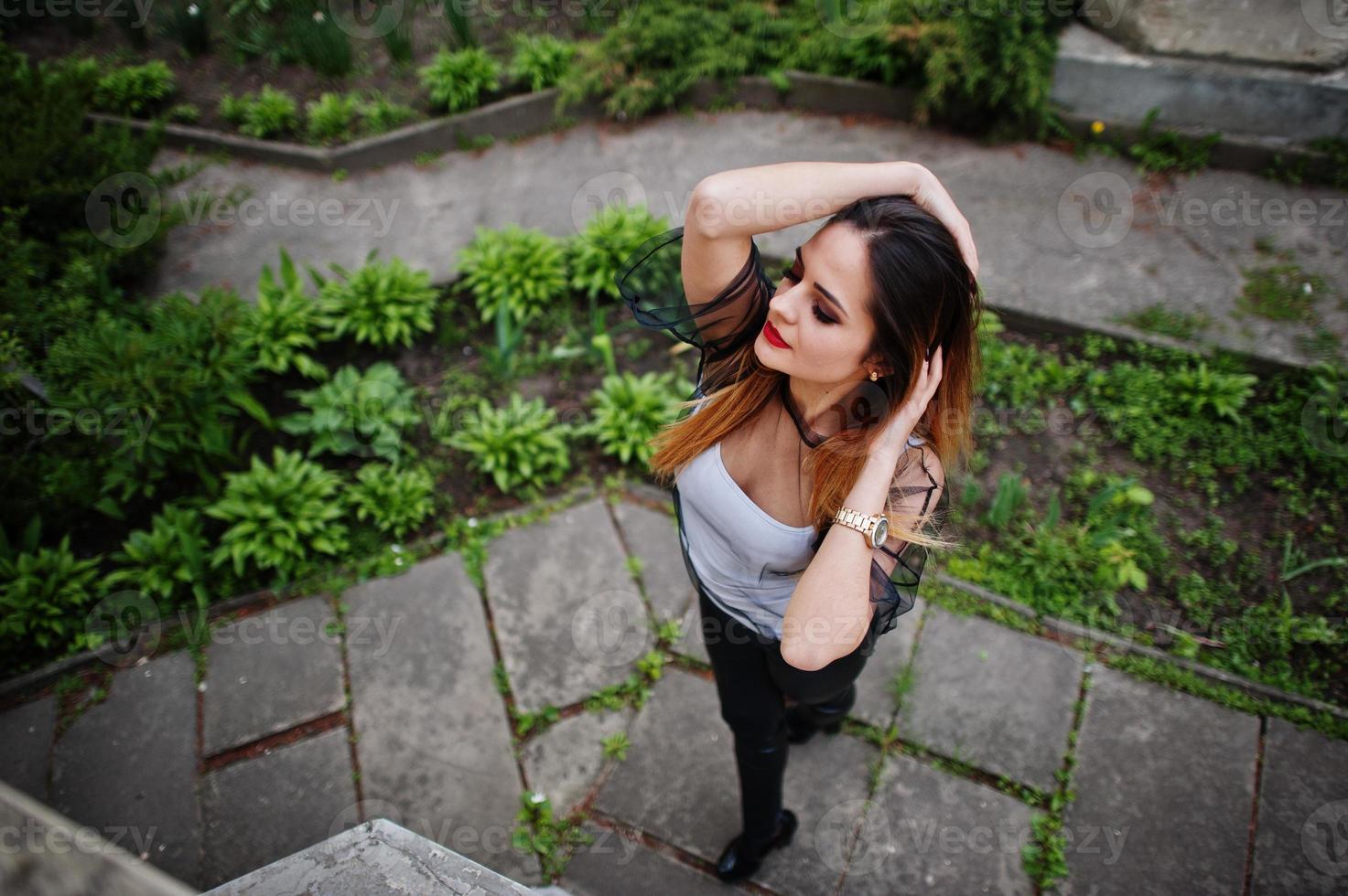 sopra la vista della donna alla moda guarda una camicia bianca, abiti neri trasparenti, pantaloni di pelle, in posa per strada. concetto di ragazza di moda. foto