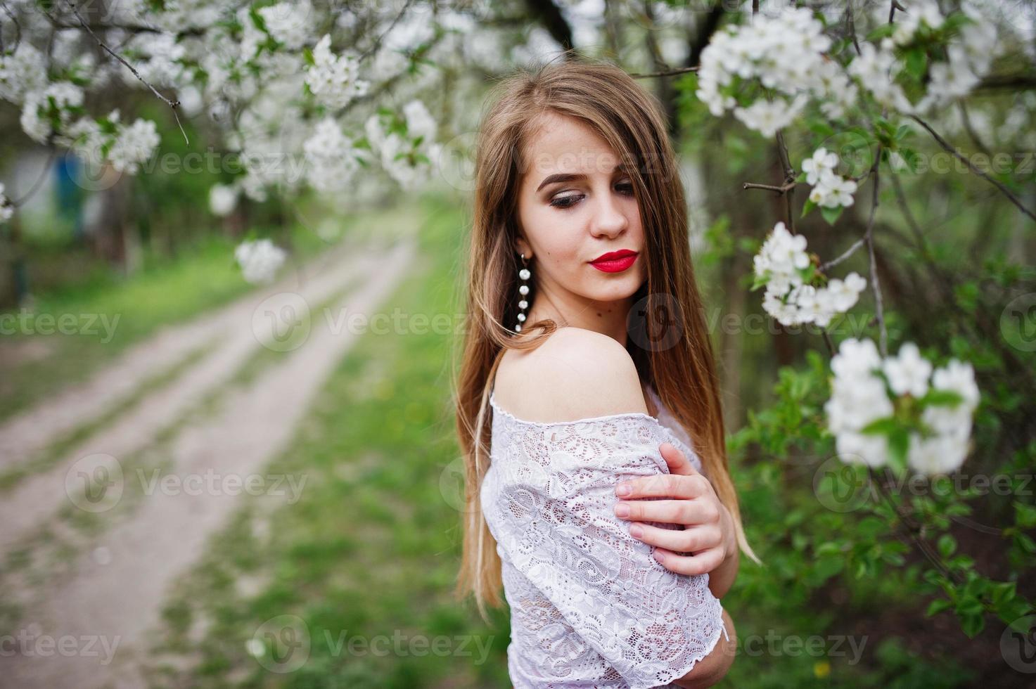 ritratto di bella ragazza con labbra rosse al giardino di fiori primaverili, indossare su abito rosso e camicetta bianca. foto