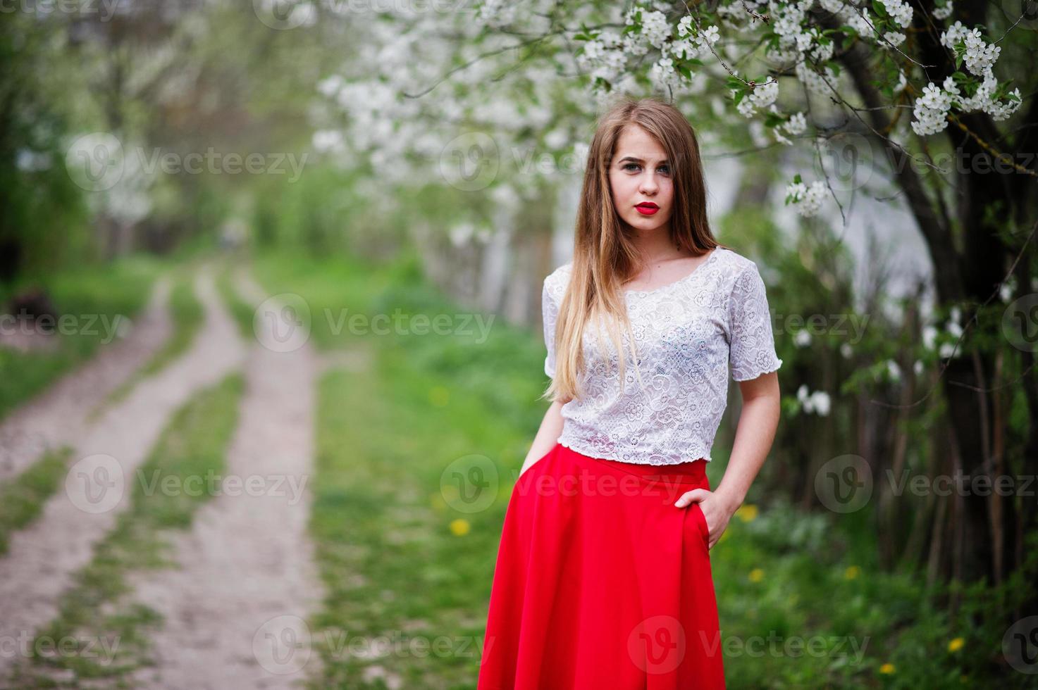 ritratto di bella ragazza con labbra rosse al giardino di fiori primaverili, indossare su abito rosso e camicetta bianca. foto