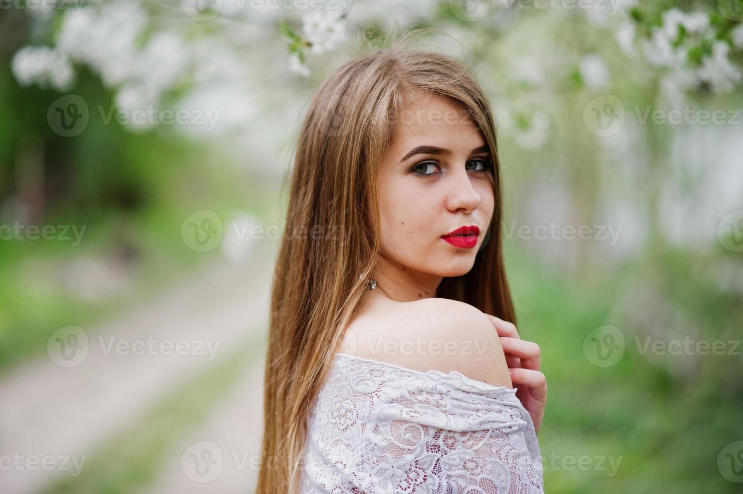 ritratto di bella ragazza con labbra rosse al giardino di fiori primaverili, indossare su abito rosso e camicetta bianca. foto