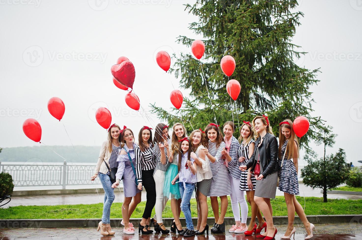 undici trecce damigelle dall'aspetto sorprendente con splendida sposa in posa con palloncini rossi a forma di cuore sul marciapiede contro il lago sullo sfondo. foto