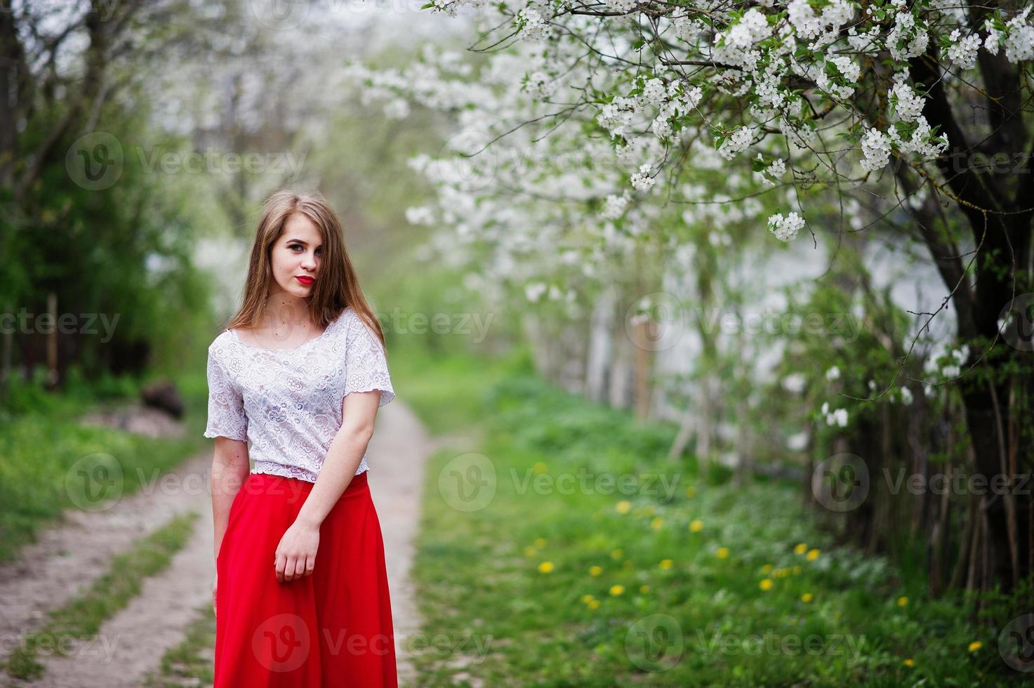 ritratto di bella ragazza con labbra rosse al giardino di fiori primaverili, indossare su abito rosso e camicetta bianca. foto