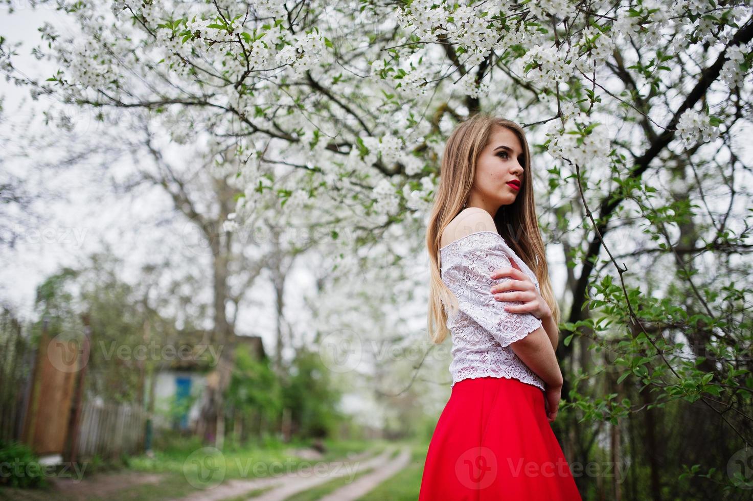 ritratto di bella ragazza con labbra rosse al giardino di fiori primaverili, indossare su abito rosso e camicetta bianca. foto