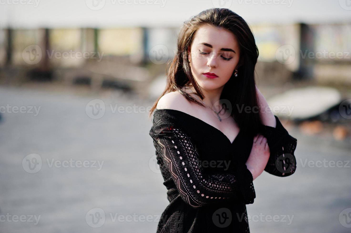 ritratto bruna ragazza con labbra rosse che indossa un abito nero poste sul tetto. modello di moda di strada. foto