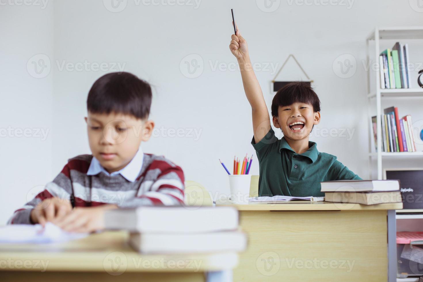 studente asiatico intelligente e attivo che alza la mano con espressione eccitata durante la lezione di classe per rispondere alla domanda foto