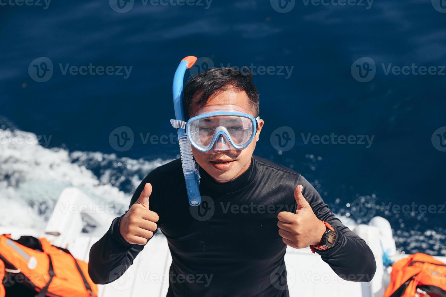 uomo asiatico in maschera per lo snorkeling che indossa una muta che dà il pollice in su pronto per lo snorkeling foto