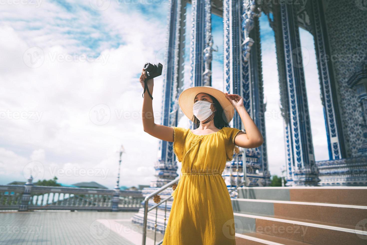 la donna asiatica adulta indossa una maschera protettiva che viaggia con la fotocamera al tempio locale asiatico il giorno. foto