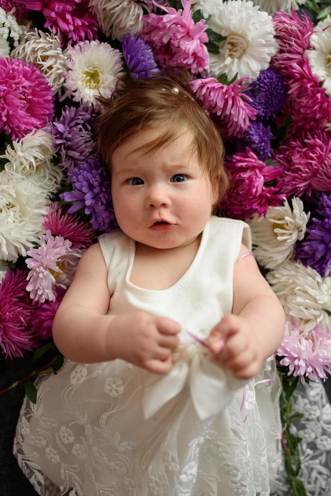 bambina in abito blu che gioca con un mazzo di tulipani rosa. bambino a casa nella scuola materna soleggiata. bambino che si diverte con i fiori foto