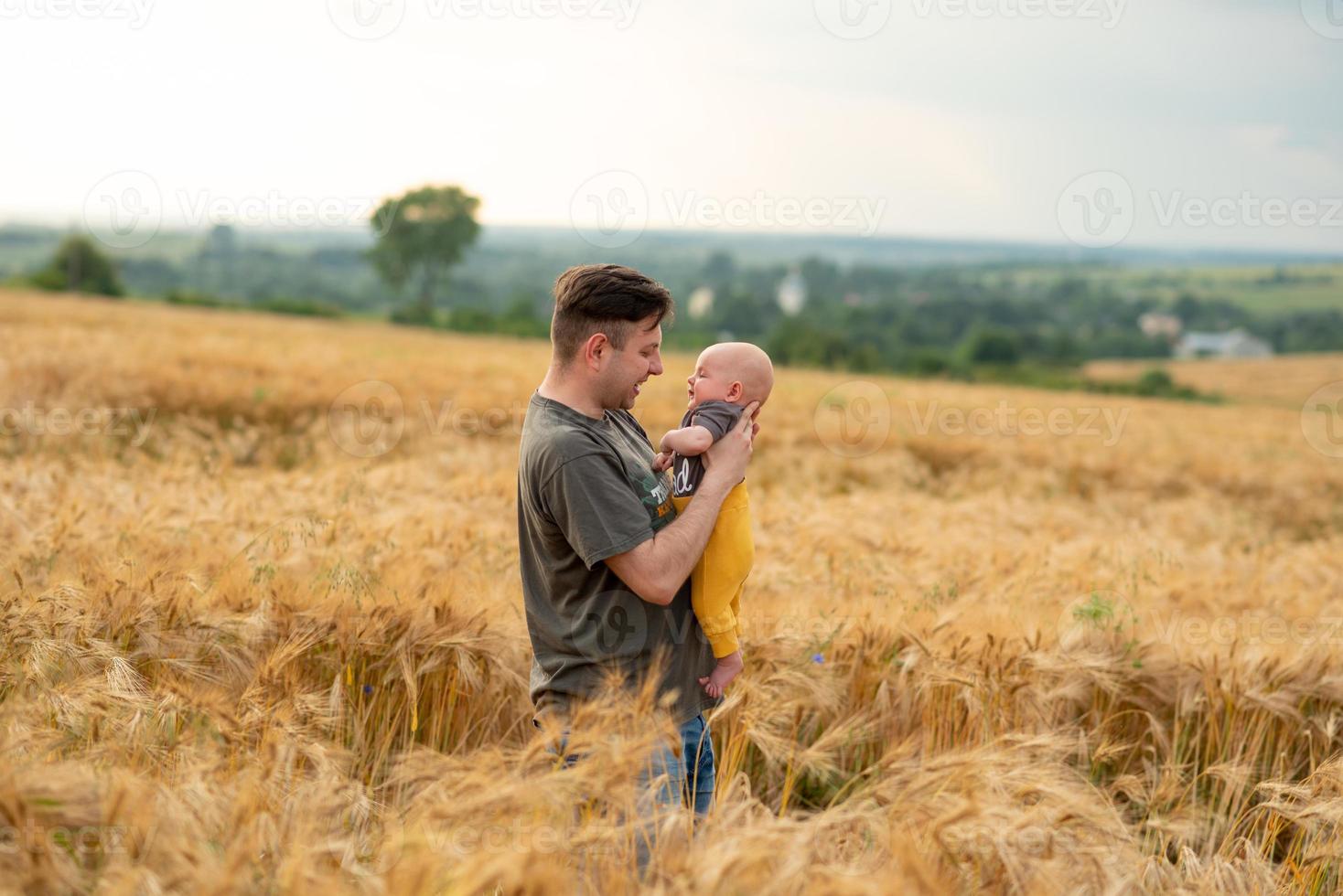 un giovane padre tiene in braccio il figlio di tre mesi. girato in un campo di grano. foto