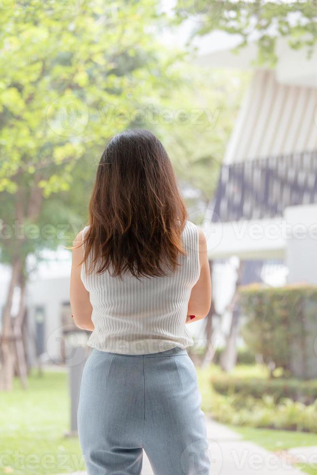 vista posteriore di giovane donna asiatica d'affari in piedi rilassata e guardando nel giardino. foto