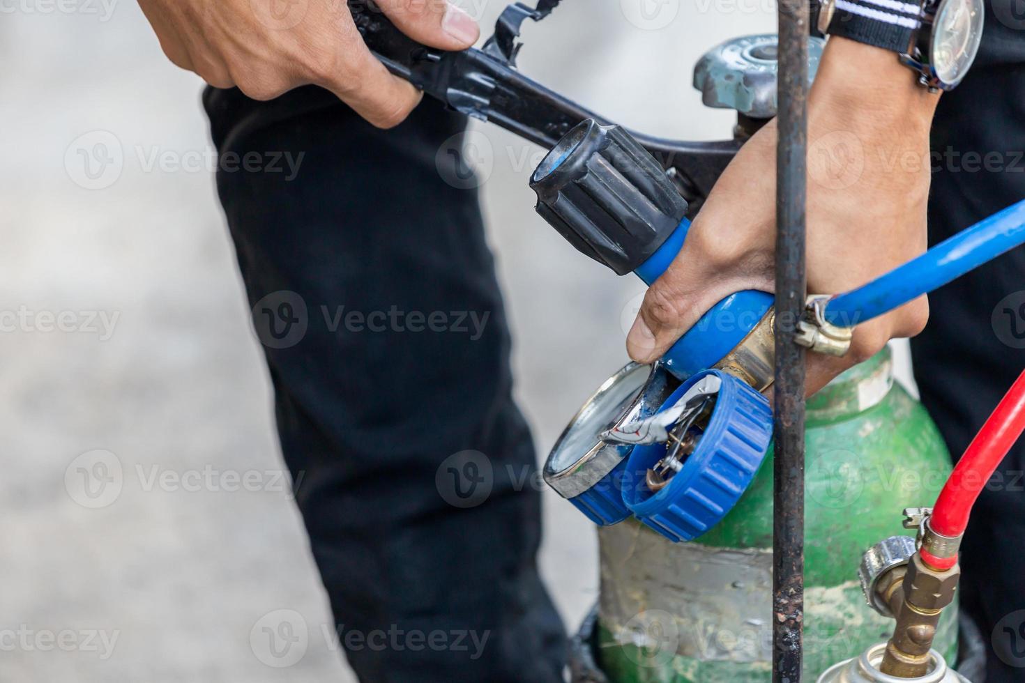 primo piano di un uomo di riparazione dell'aria condizionata, installare un manometro sui gas combustibili e sul serbatoio di ossigeno per saldare o tagliare metalli, saldatura a ossitaglio e processi di taglio a ossitaglio foto