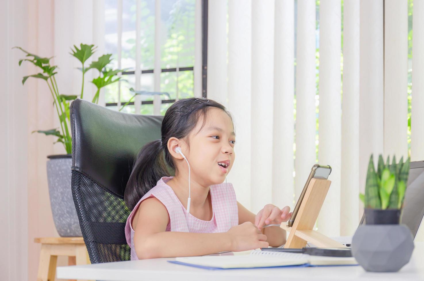 bambina allegra sorridente e mentre utilizza laptop e auricolare wireless per videochiamate, istruzione e concetto di apprendimento a distanza foto