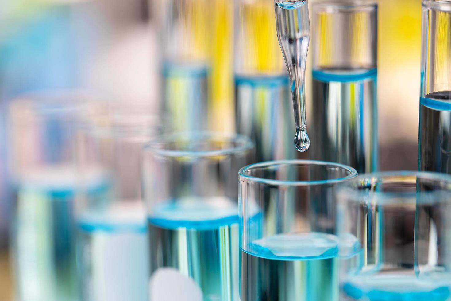 goccia di liquido blu chiaro dal contagocce che cade nella provetta in laboratorio con sfondo sfocato di colore brillante foto