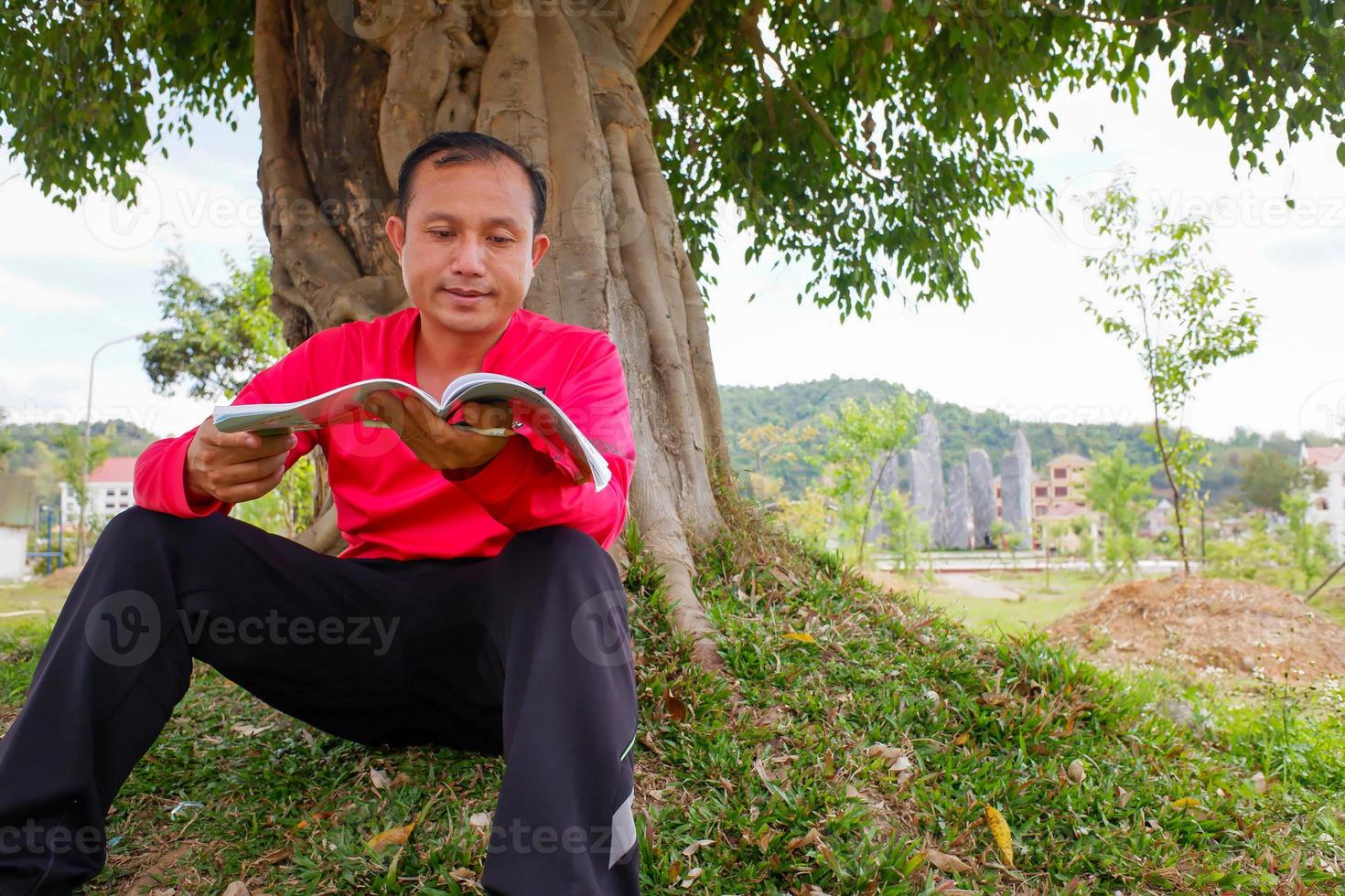 un giovane che legge un libro che si lava la mano fuori archiviato sotto l'albero. foto