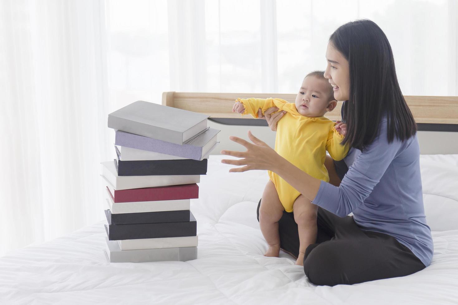 una madre asiatica ha aiutato il suo bambino a stare in piedi. e c'era una pila di libri posta accanto a lei sul letto. foto