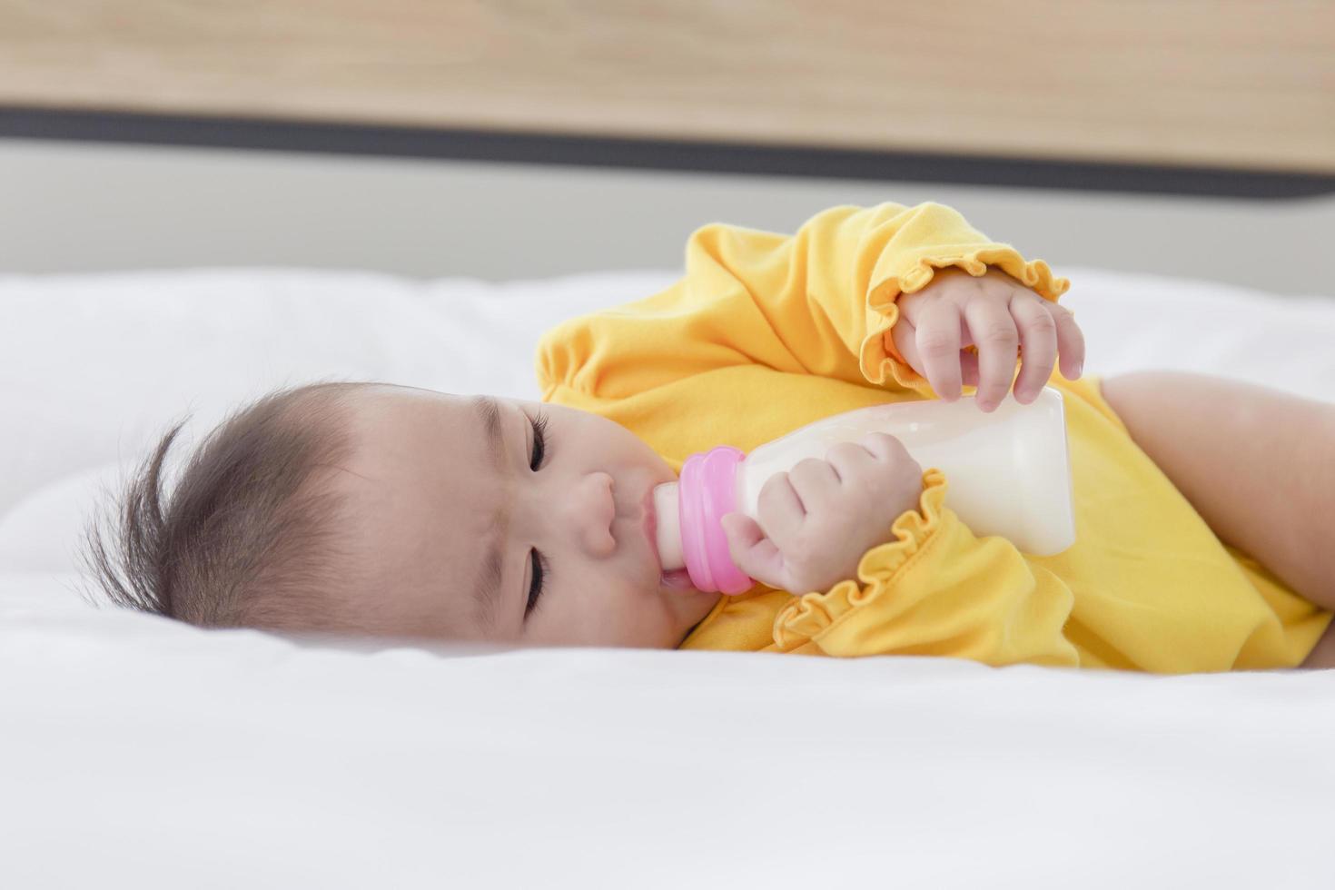 un bambino asiatico dorme sul letto e succhia il latte in bottiglia. foto