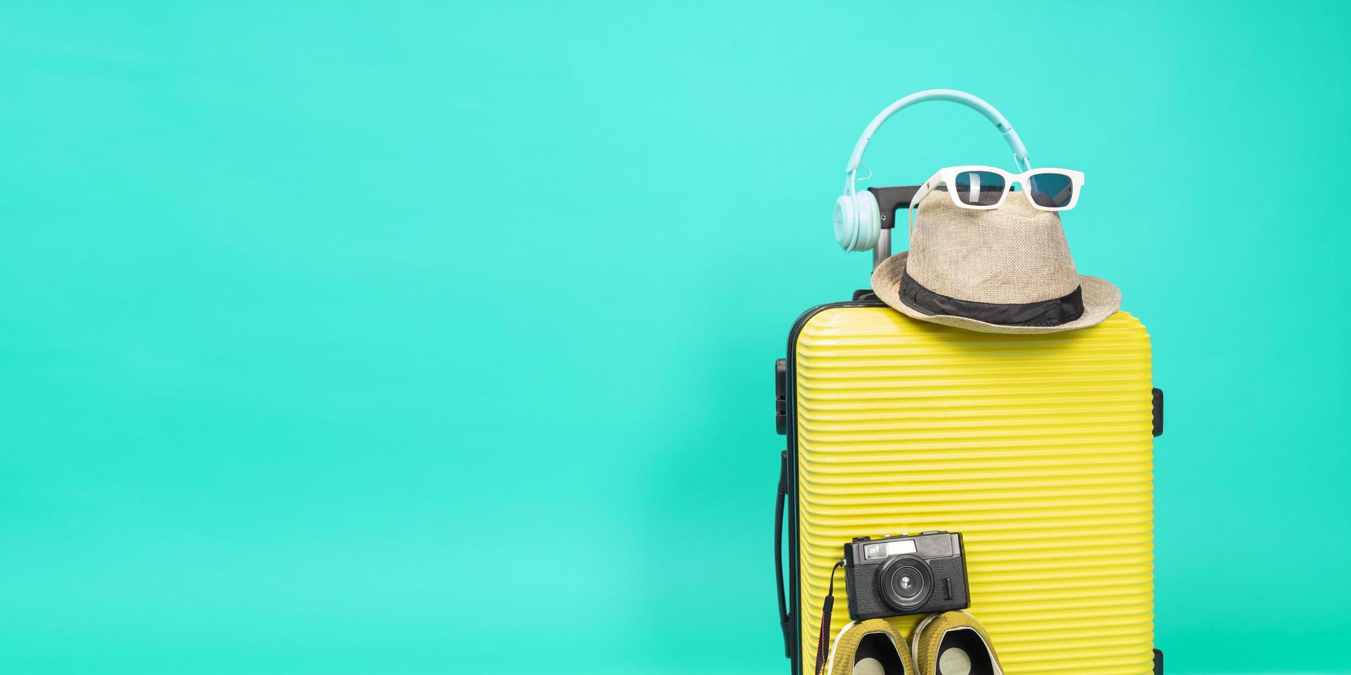 valigia gialla con occhiali da sole, cappello e fotocamera su sfondo blu pastello. concetto di viaggio. stile minimale foto