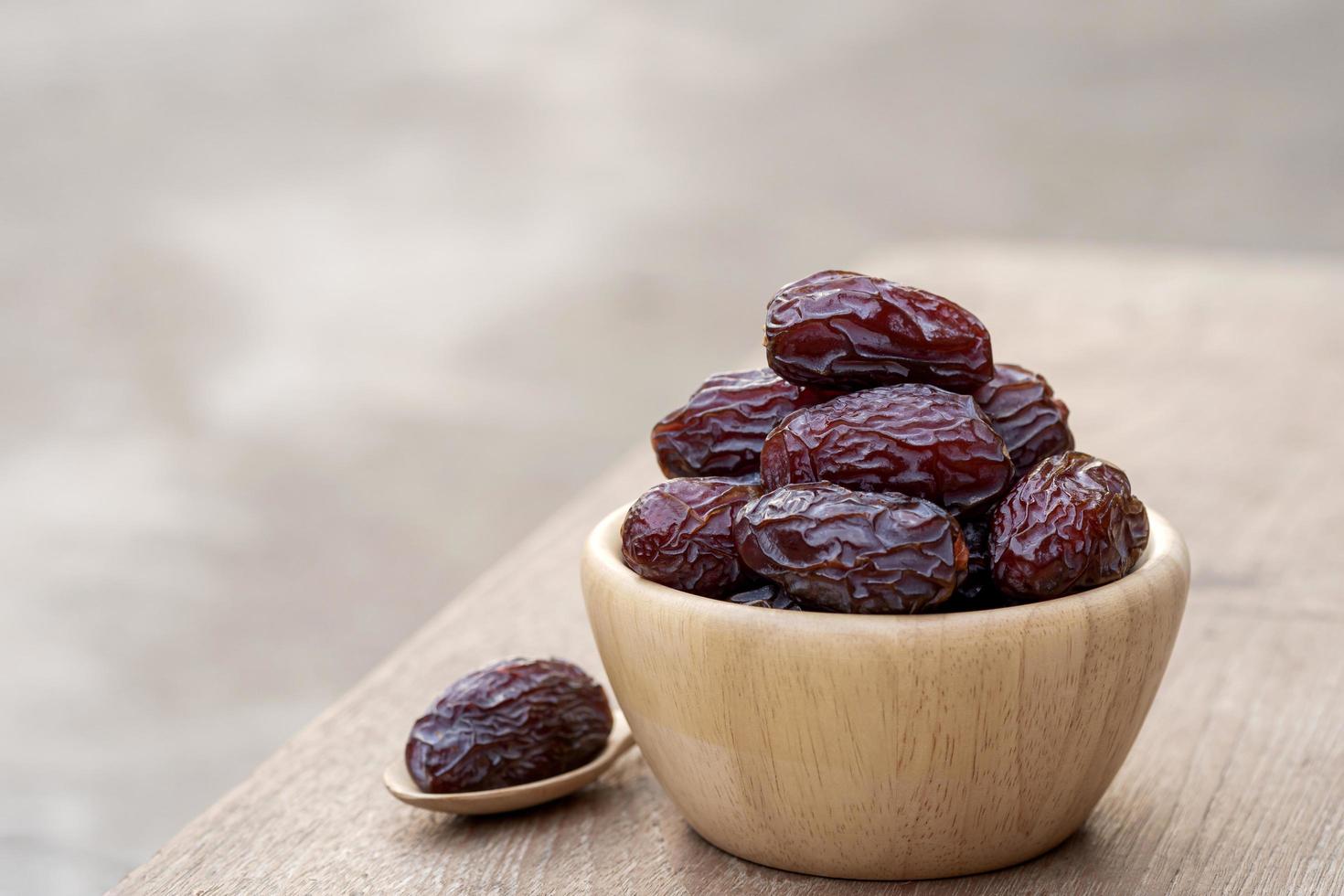 medjool datteri o datteri frutta in ciotola di legno e cucchiaio sul tavolo, questo frutto è altamente nutriente e viene comunemente consumato durante il digiuno o il ramadan. foto