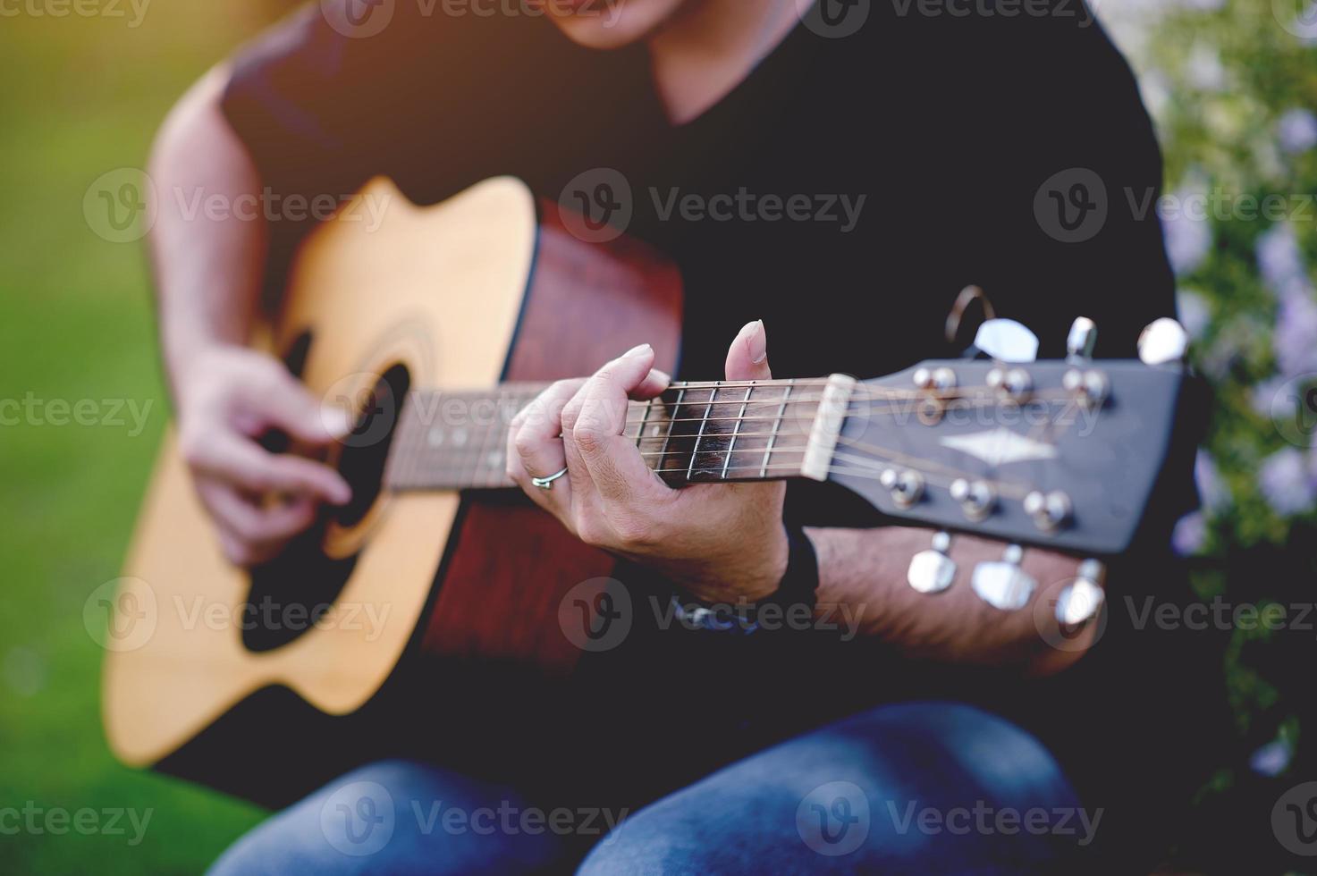 immagine di un chitarrista, un giovane che suona una chitarra mentre è seduto in un giardino naturale, concetto musicale foto