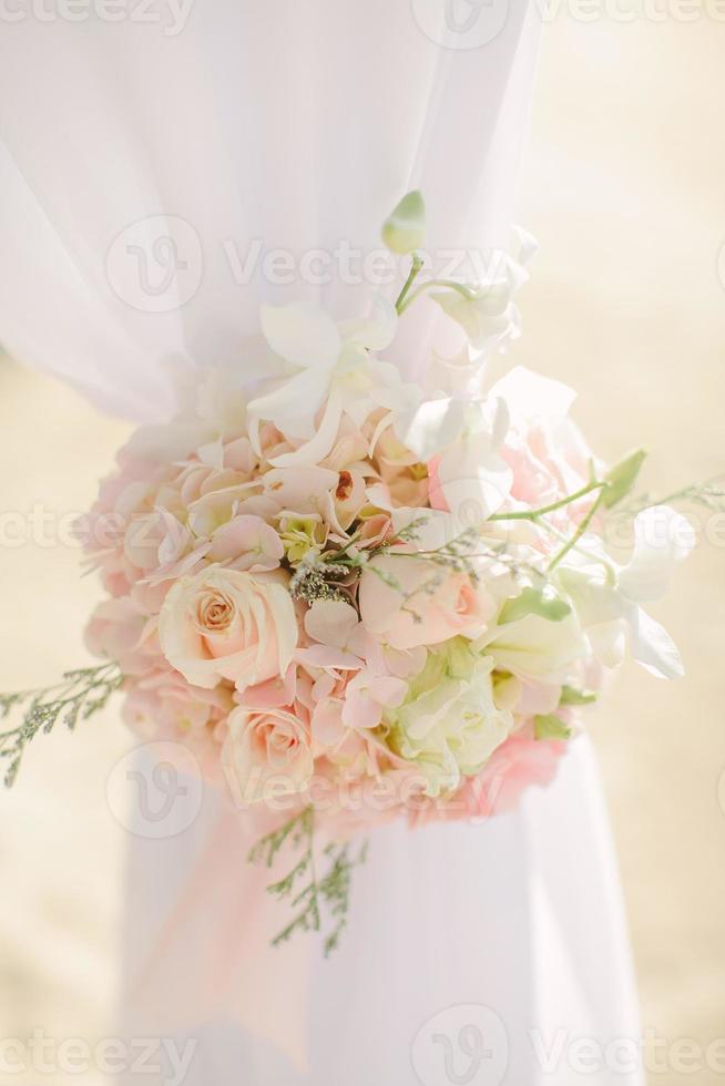 composizione floreale colorata rosa e verde chiaro legata ad un arco in una cerimonia di matrimonio foto