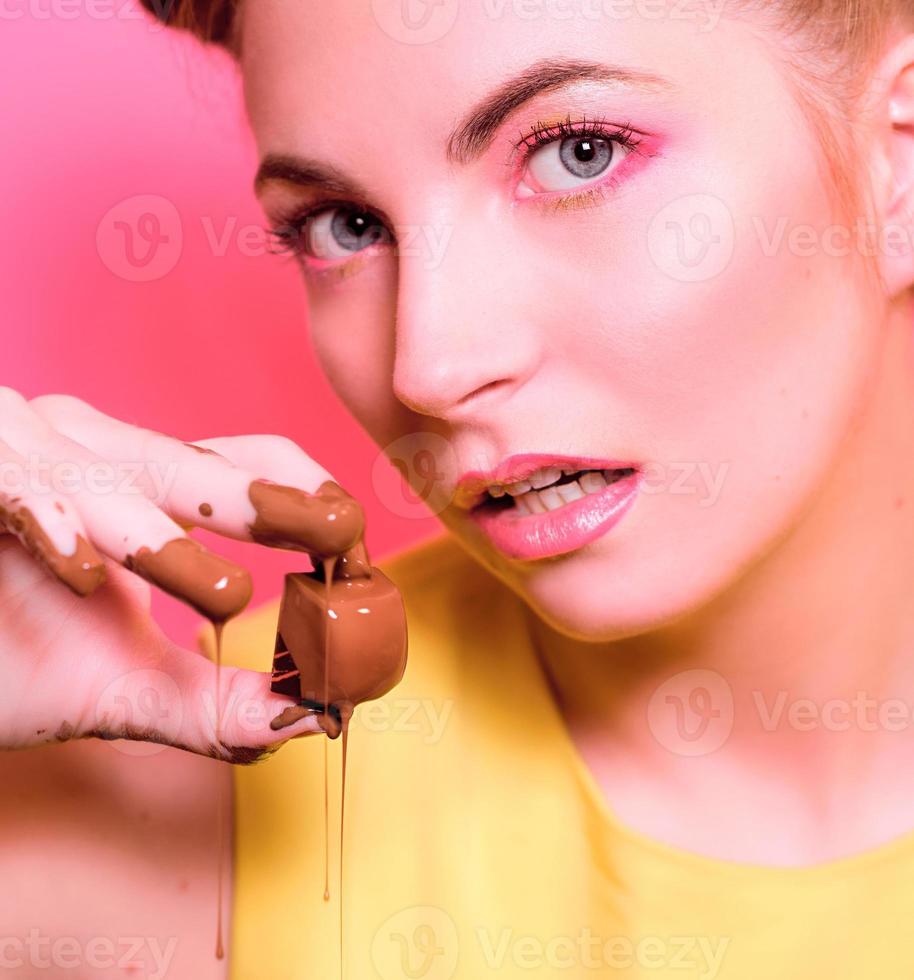 ritratto di giovane donna bionda carina attraente con caramelle al cioccolato tra le dita foto