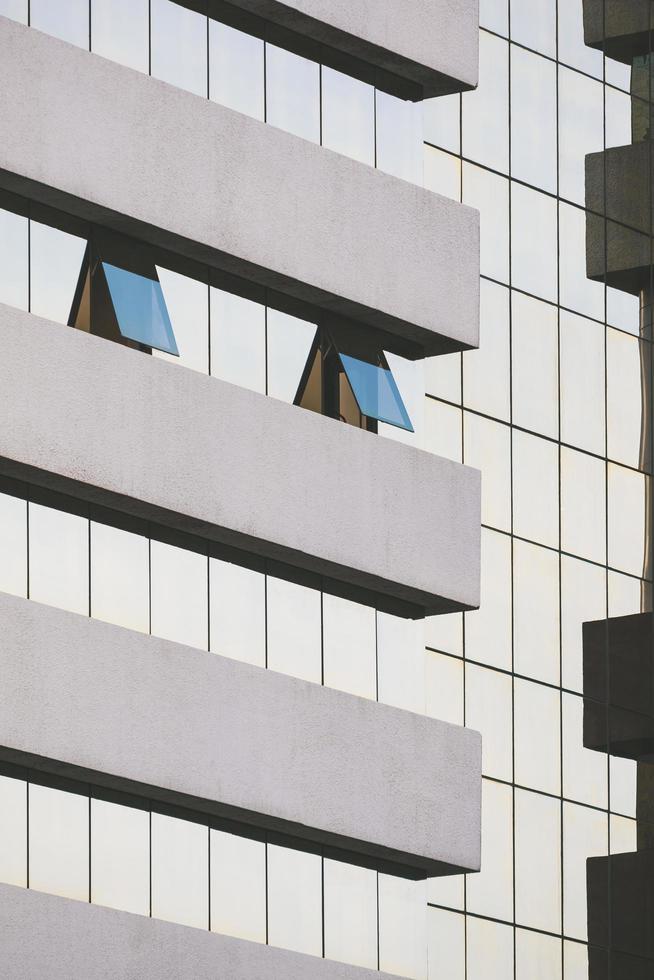 concentrarsi su 2 finestre di vetro blu che si aprono sulla moderna parete di un edificio per uffici in vetro alto con cornice verticale foto