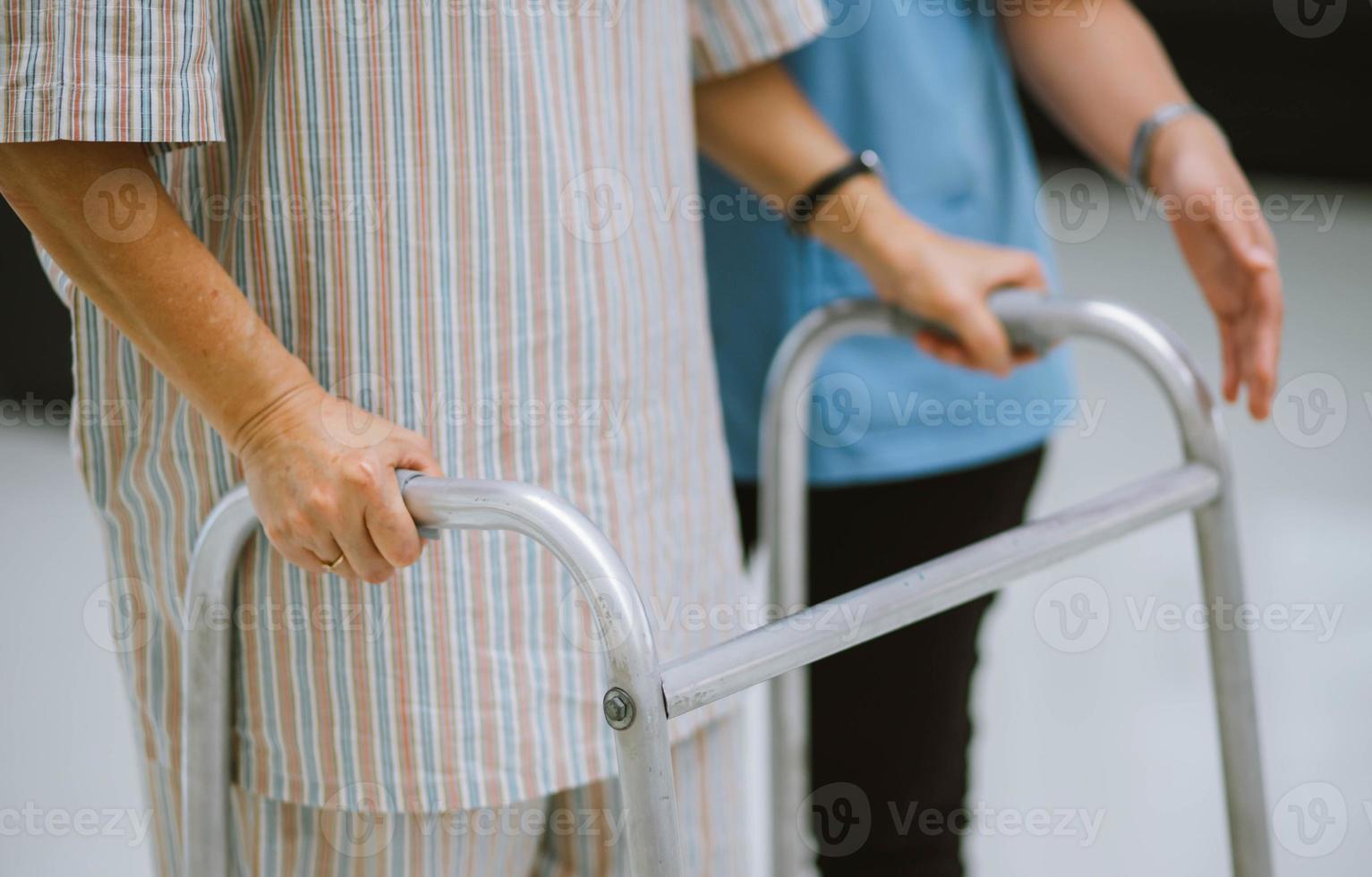 primo piano giovane fisioterapista che aiuta il paziente anziano a usare il deambulatore durante la riabilitazione foto