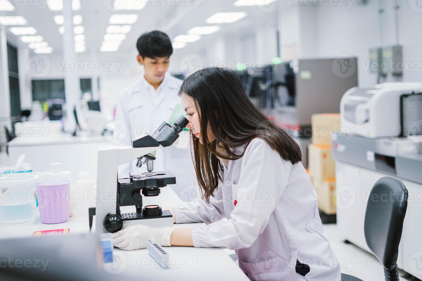 due scienziati medici che lavorano in laboratorio medico, giovane scienziata che guarda al microscopio. selezionare il focus in una giovane scienziata foto