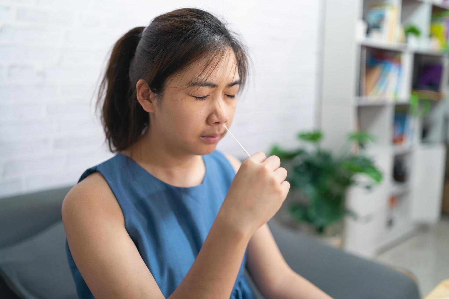 donna asiatica che tiene la mano, autotest del kit antigene, test del tampone nasale per possibile infezione da coronavirus, covid-19 a casa. concetto di pandemia di malattia covid-19. foto