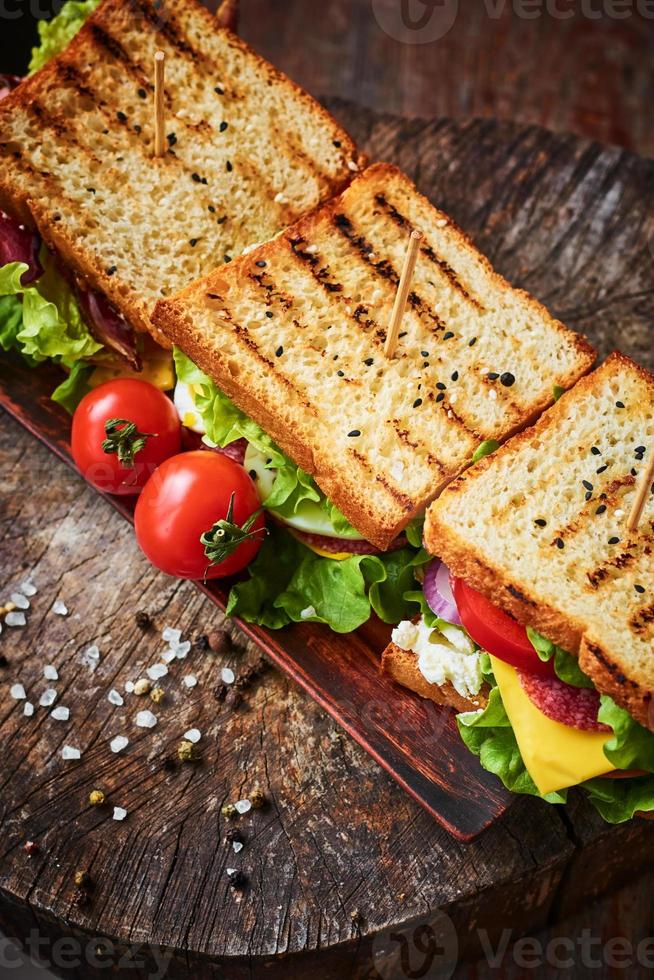 panino fatto in casa con prosciutto, lattuga, formaggio e pomodoro su fondo di legno, vista dall'alto foto