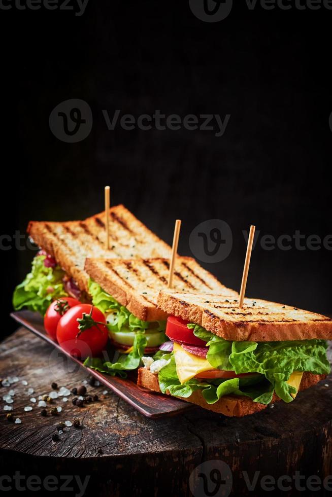 panino fatto in casa con prosciutto, lattuga, formaggio e pomodoro su fondo di legno foto