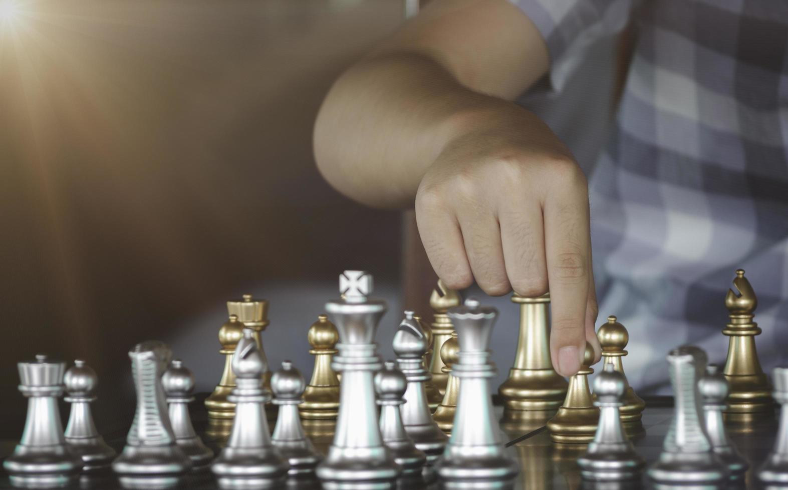 mano uomo d'affari muovendo il cavaliere d'oro che combatte il cavaliere d'argento con scintille di fuoco scacchi sulla scacchiera per vincere con successo nella competizione. strategia di gestione o leadership e concetto di lavoro di squadra. foto