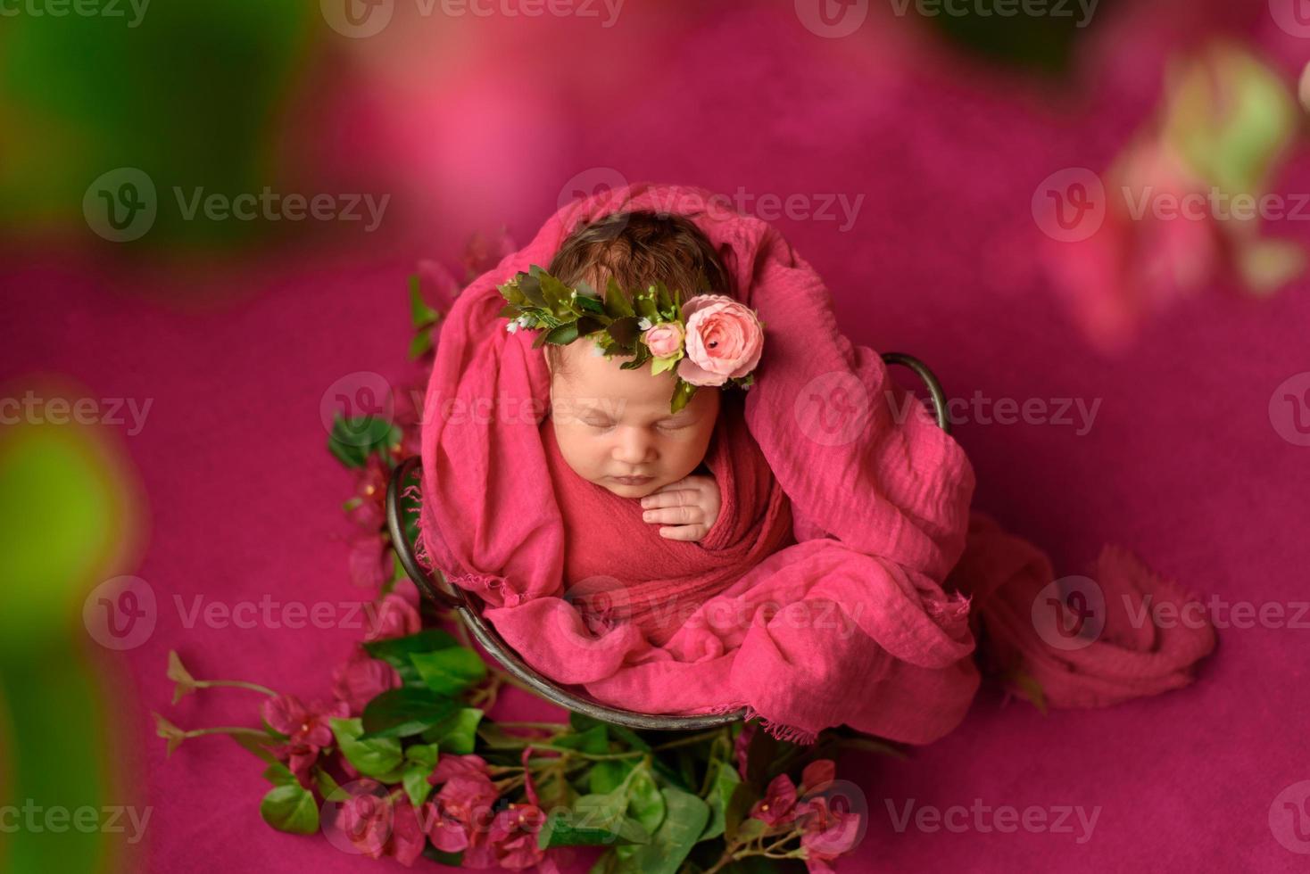 Ritratto in primo piano di una ragazza appena nata carina che dorme avvolta in una morbida coperta viola, indossando un elegante fiore di testa, concetto di moda per bambini foto