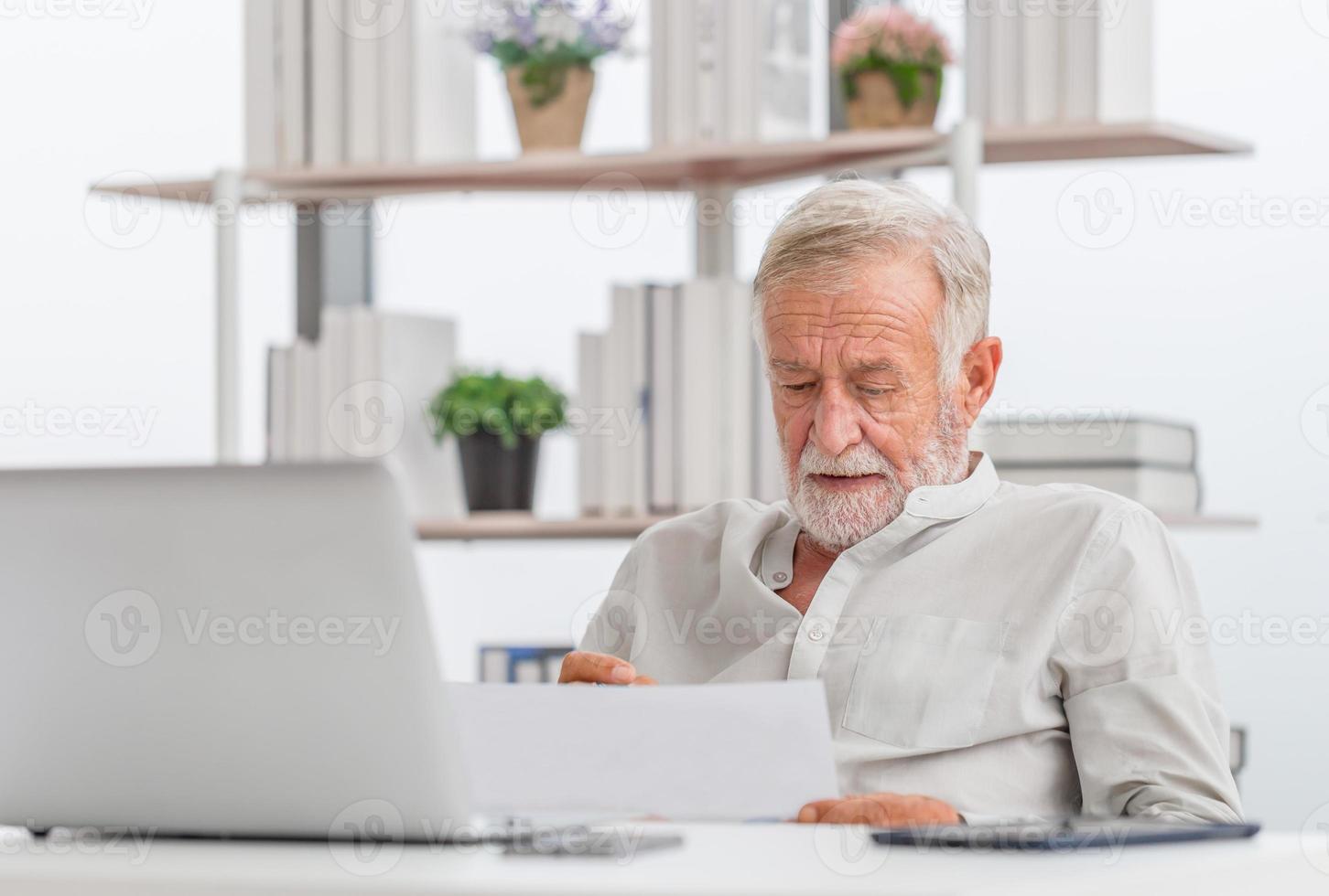 uomo anziano preoccupato che controlla le bollette, vecchi documenti di lettura di famiglia anziani in pensione, uomo maturo in soggiorno con laptop foto