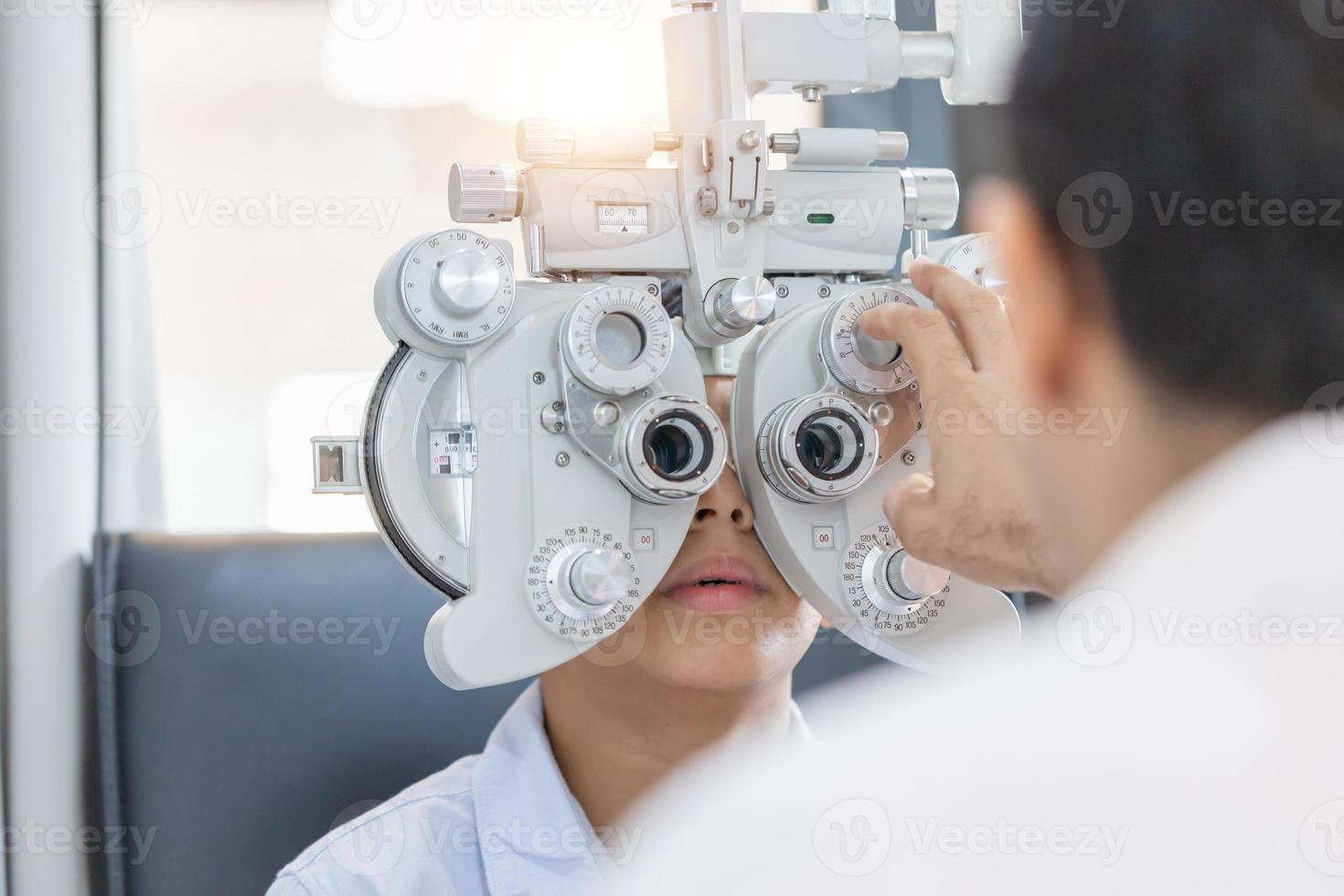 ragazzo che fa il test della vista che controlla l'esame con l'ottico optometrista in negozio di ottica, optometrista che esegue il test della vista per il paziente bambino in clinica foto