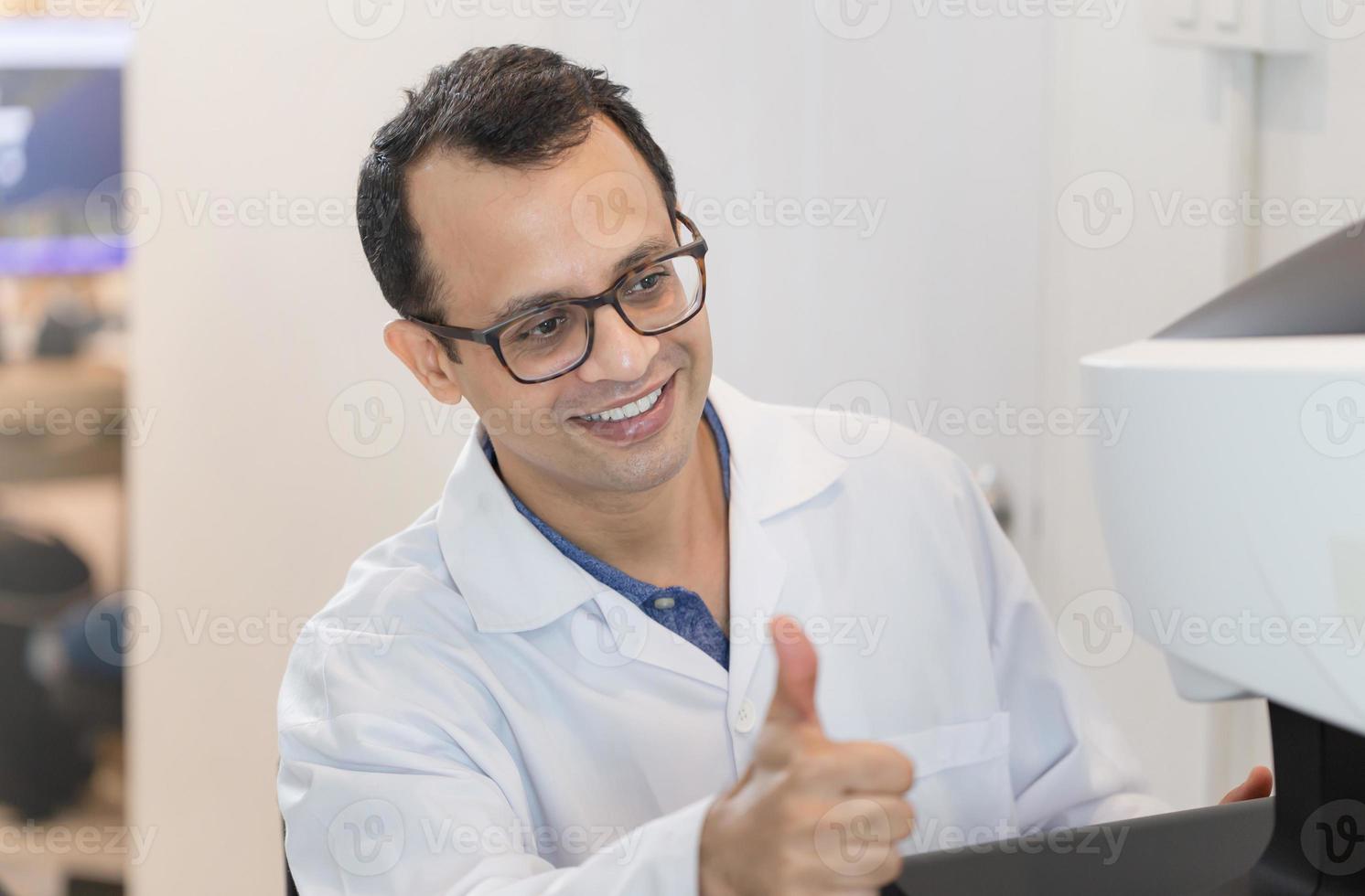 optometrista felice che mostra i pollici in su nel negozio di ottica, optometrista indiano sorridente foto