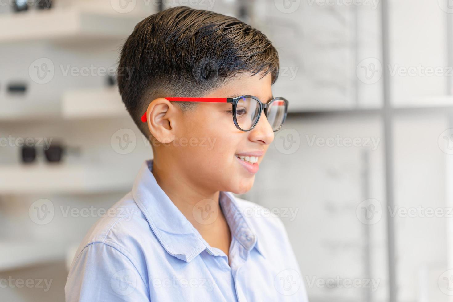 ragazzo indiano sorridente che sceglie gli occhiali nel negozio di ottica, ritratto di un bambino di etnia di razza mista che indossa gli occhiali nel negozio di ottica foto