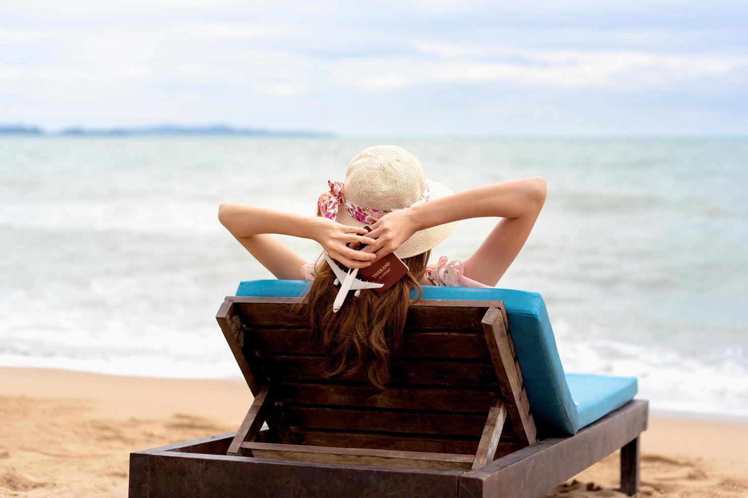 donna del viaggiatore che si rilassa alla spiaggia che tiene il passaporto e il modello dell'aeroplano. foto