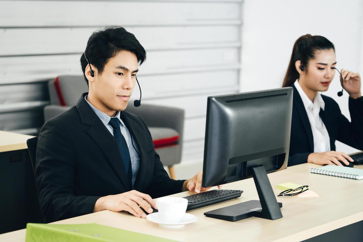 sorriso positivo giovane personale aziendale uomo asiatico utilizzando cuffie e computer per il supporto. foto