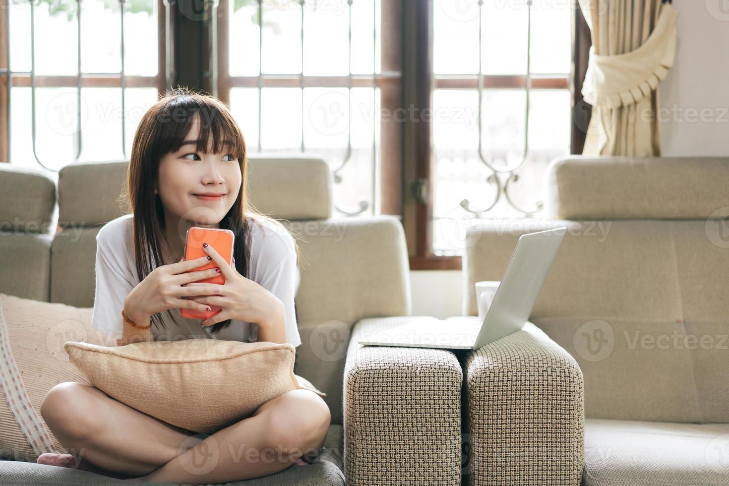 felice sorriso asiatico adolescente donna tenere smart phone in soggiorno. foto