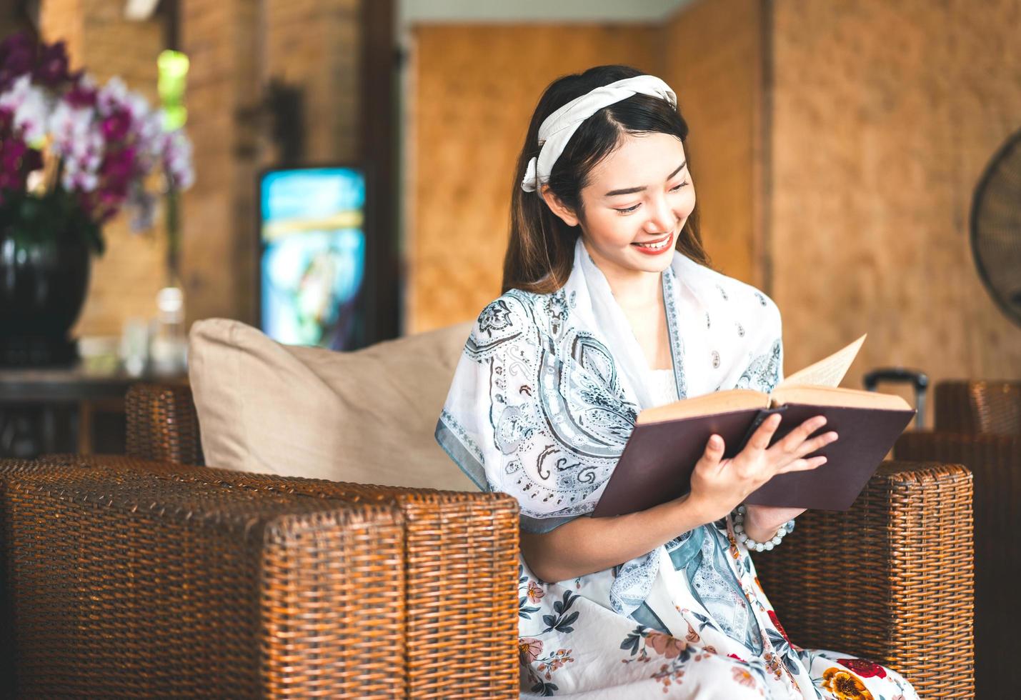 donna asiatica che legge un libro sul divano di vimini. foto