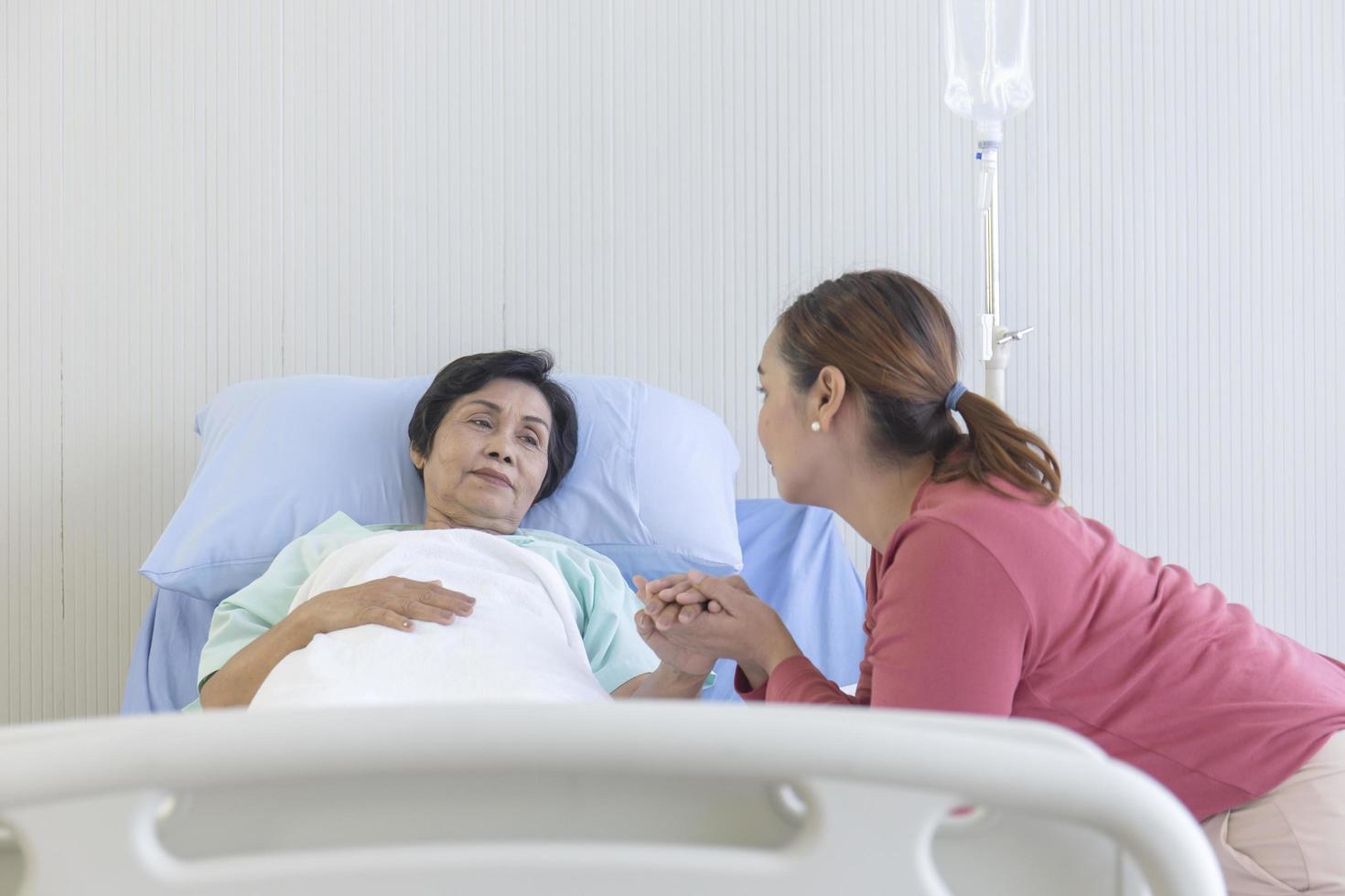 una donna asiatica le tiene la mano per incoraggiare sua madre a dormire in un letto d'ospedale con calore e cura. foto