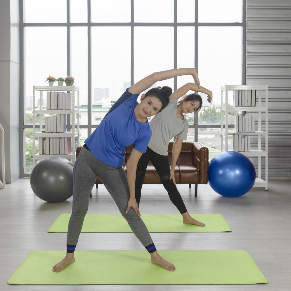 2 femmine asiatiche una donna di mezza età sta facendo yoga su un tappetino di gomma nella sua casa. foto