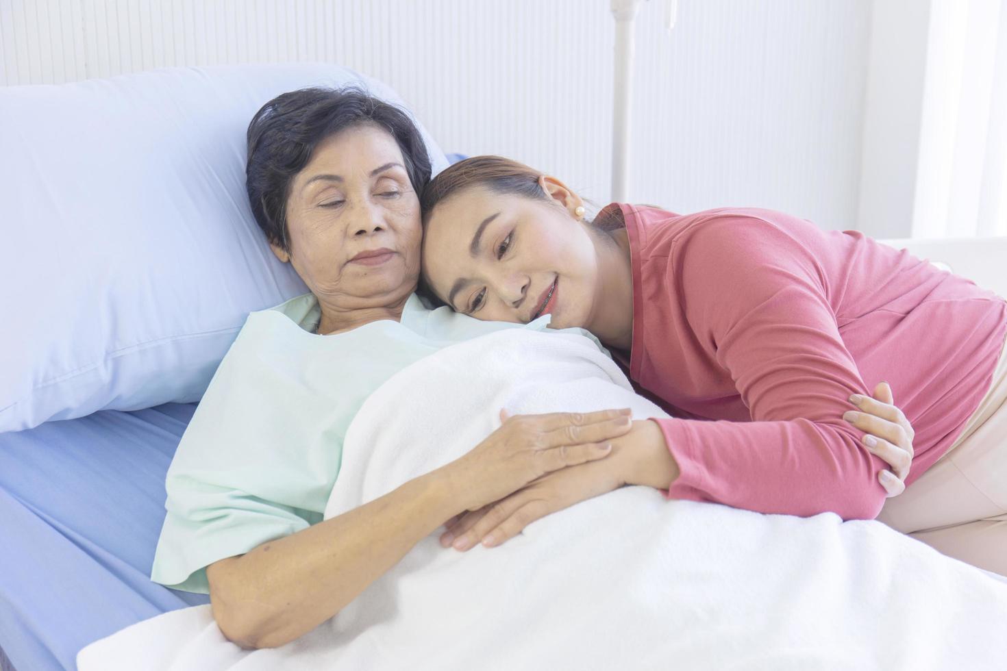 una donna asiatica abbraccia la madre che si sta riprendendo su un letto d'ospedale. foto