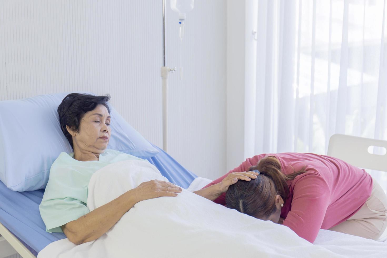 una madre malata a letto, una donna asiatica ha strofinato la testa della figlia addormentata nel letto d'ospedale foto